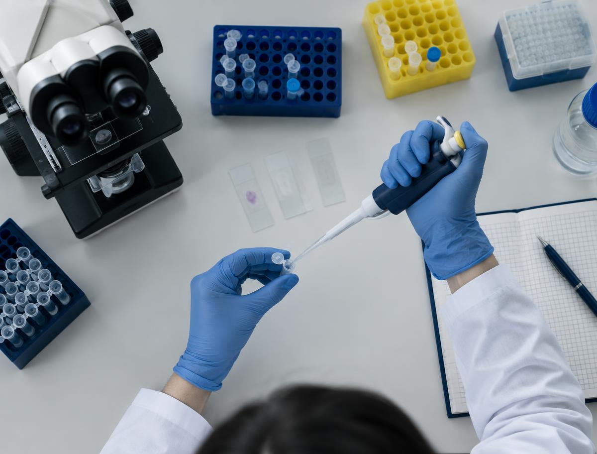 Gloved hands pipetting beside a microscope and sample racks
